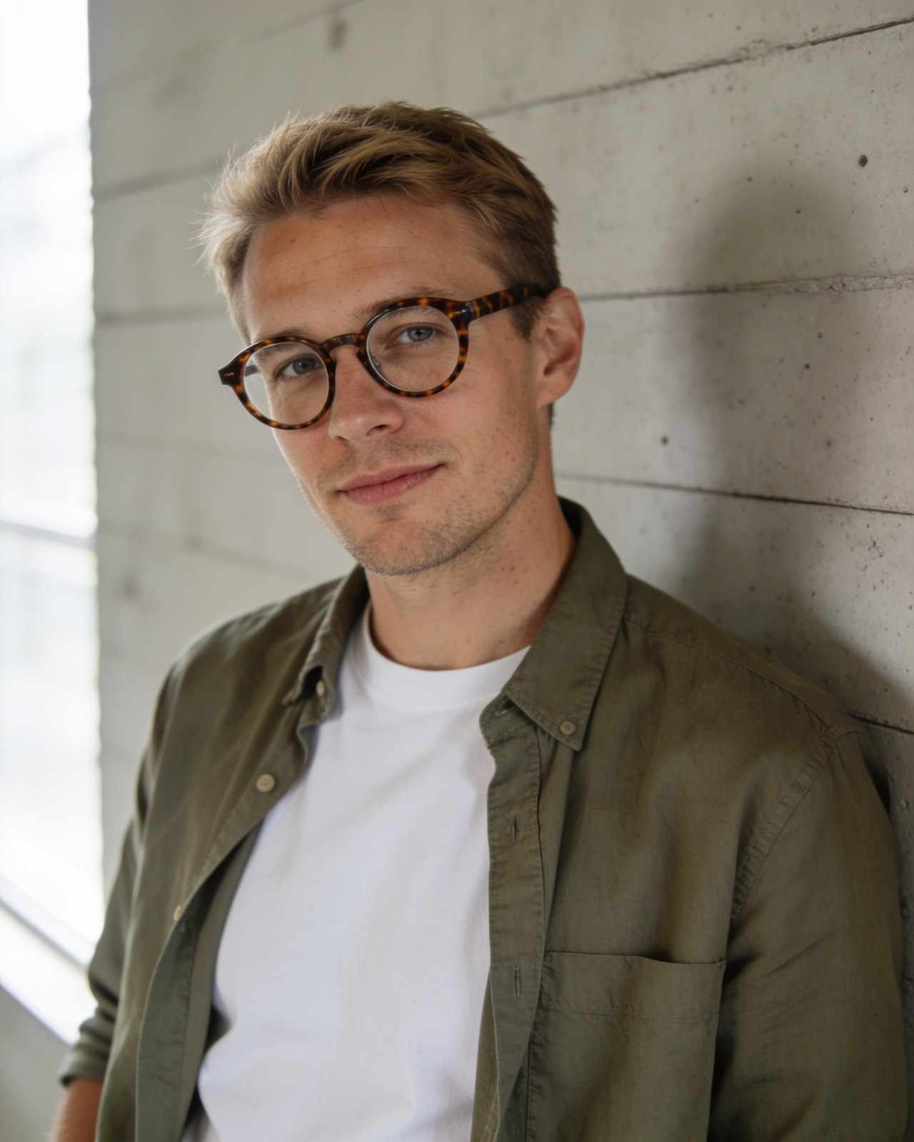 Felix Brandt, a man in his thirties with round glasses and an olive overshirt, against a concrete wall