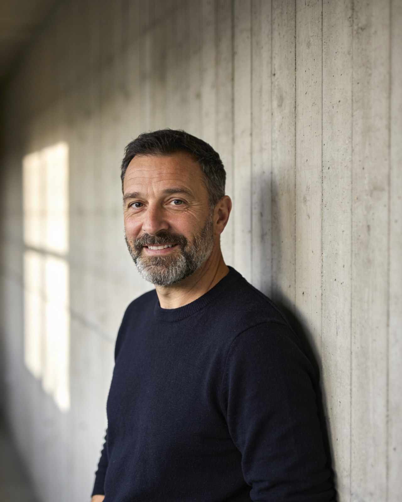 Jonah Varga, a bearded man in his forties in a navy jumper, against a concrete wall