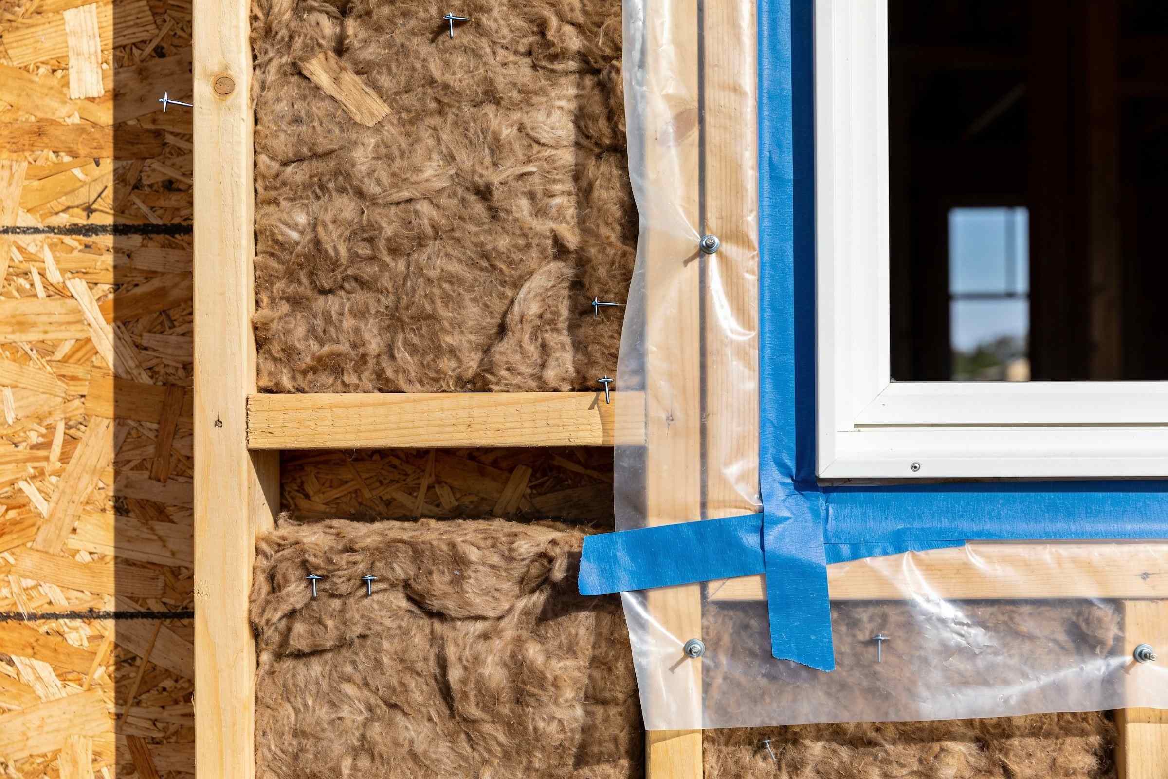 A timber stud wall on site filled with wood-fibre insulation, an airtight membrane taped neatly at the joints